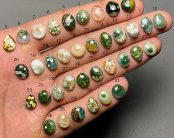 Könnte beinhalten: Eine Sammlung von 36 polierten Edelsteinen in verschiedenen Formen und Farben, darunter Grün, Weiß, Gelb und Braun. Die Edelsteine sind von 1 bis 36 nummeriert und werden auf einer Hand präsentiert.