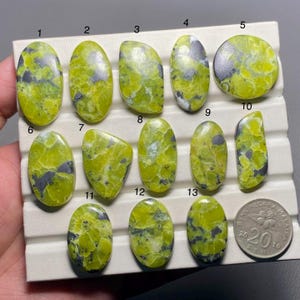 May include: Thirteen green and black cabochon gemstones arranged in rows on a white display card. The gemstones are numbered 1 through 13. A Malaysian coin is in the lower right corner of the image.