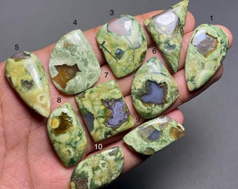 May include: Ten green, brown, and white cabochon stones with various shapes and patterns. The stones are arranged on a hand.