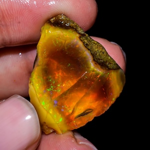 May include: A rough, orange, yellow, and green opal gemstone with iridescent flashes of color.