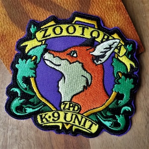 May include: Embroidered patch featuring a fox head with green and yellow accents. The patch has the text "Zootopia" and "K9 Unit" on it.