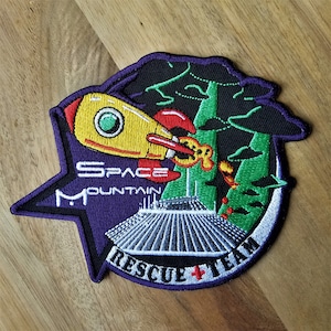 May include: Purple embroidered patch with a yellow rocket ship, green trees, and the text "Space Mountain Rescue Team".