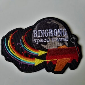 May include: Embroidered patch with the words "BINGBONG space travel" above a graphic of a rocket ship and a rainbow trail. The patch is black with colorful accents and a white background.