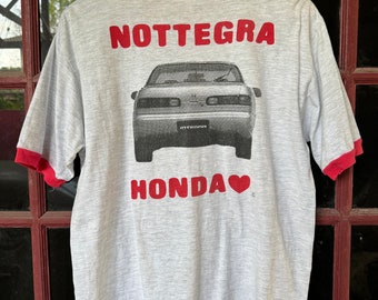 May include: Grey t-shirt with a red ringer. The back of the shirt features a black and white image of a Honda Integra with the text "NOTTEGRA" and "HONDA" with a red heart.