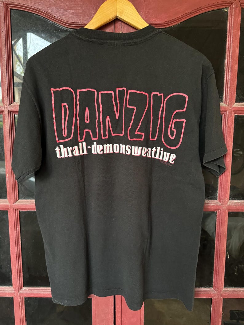 May include: Black t-shirt with a red graphic print of the word "DANZIG" and the text "thrall-demonsweatlive" underneath.