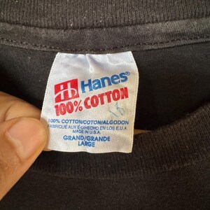 May include: A black Hanes t-shirt with a white tag that reads "100% Cotton" and "Hanes". The tag also includes the text "100% Cotton/Coton/Algodon", "Fabrique aux E-U/Hecho en los E.U.A", "Made in U.S.A.", "Grand/Grande", and "Large".