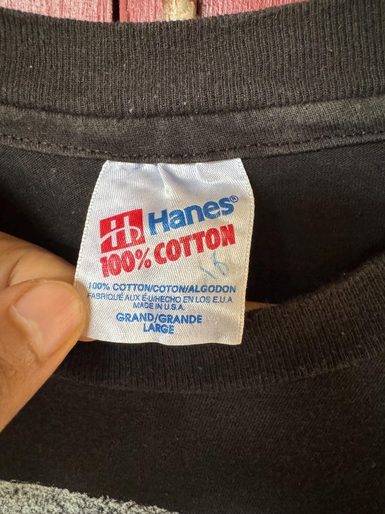 May include: A black Hanes t-shirt with a white tag that reads "100% Cotton" and "Hanes". The tag also includes the text "100% Cotton/Coton/Algodon", "Fabrique aux E-U/Hecho en los E.U.A", "Made in U.S.A.", "Grand/Grande", and "Large".
