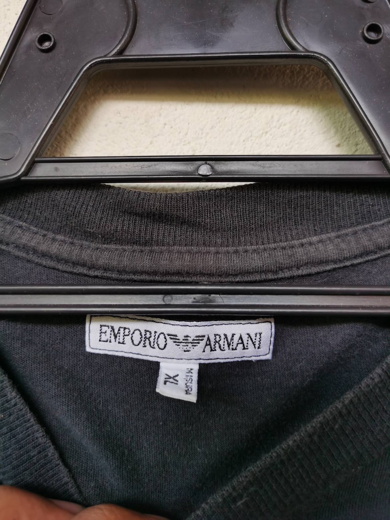 Puede incluir: Camiseta negra con una etiqueta blanca que dice "EMPORIO ARMANI" y "XL" en negro.