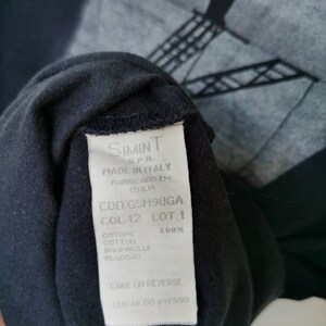 Puede incluir: Etiqueta blanca con texto negro en una camiseta negra. La etiqueta dice "SIMINT S.P.A. MADE IN ITALY FABRICADO EM ITALIA COD.GSH98GA COL.12 LOT.1 COTONE 100% COTTON BAUMWOLLE ALGOD&Atilde;O CARE ON REVERSE CUIDAR DO AVESSO"