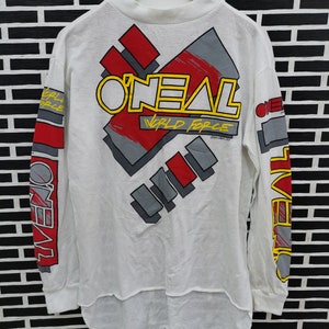 May include: White long-sleeve shirt with a red, yellow, and gray graphic print of the word "ONEAL" and the text "WORLD FORCE".