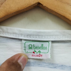 May include: White striped t-shirt with a green and white Benetton label. The label says "100% cotton".