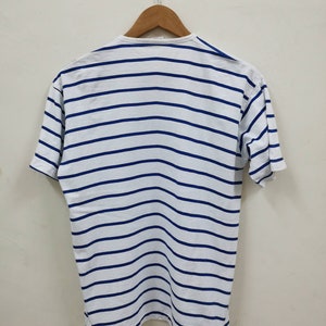 May include: White striped t-shirt with blue stripes. The shirt is hanging on a wooden hanger.