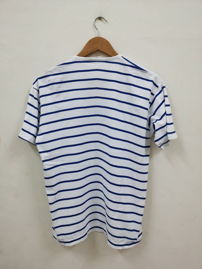 May include: White striped t-shirt with blue stripes. The shirt is hanging on a wooden hanger.