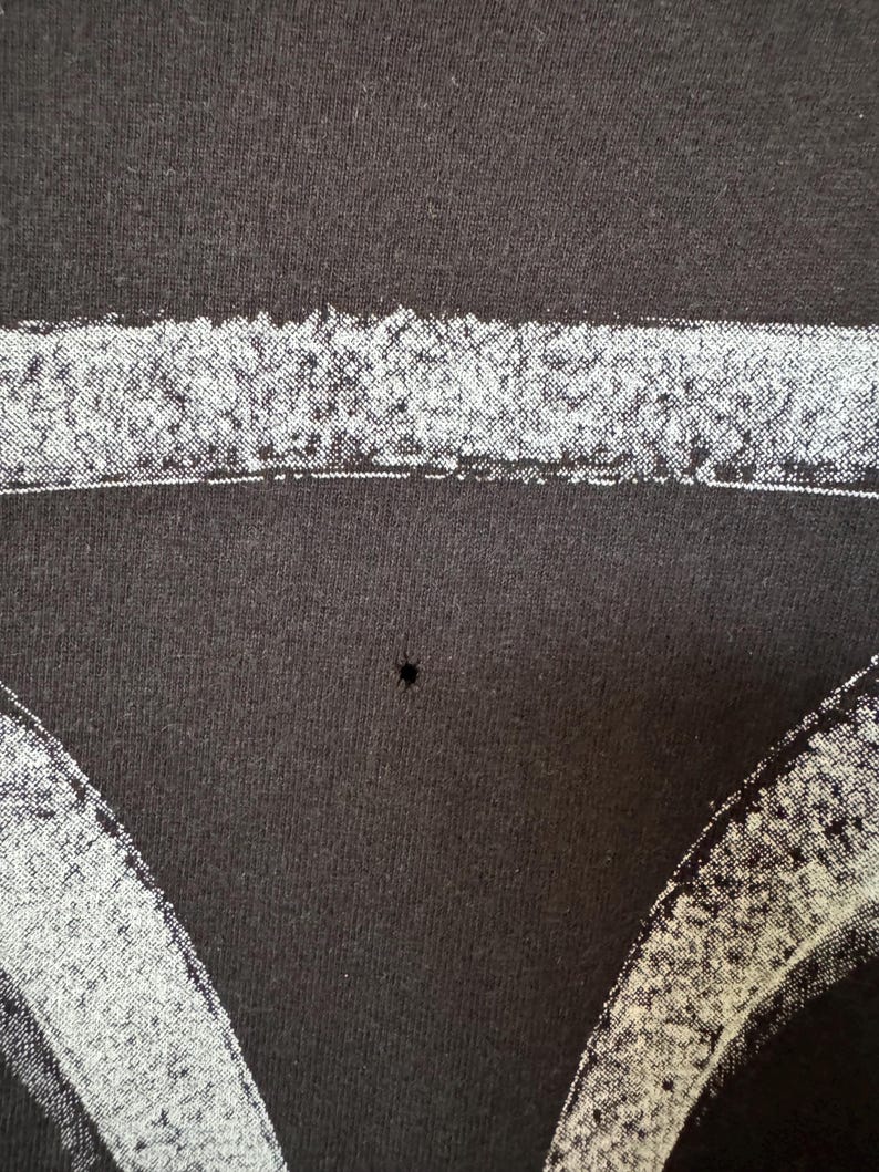 May include: Black t-shirt with a white graphic print of a skull, featuring a small hole in the fabric.