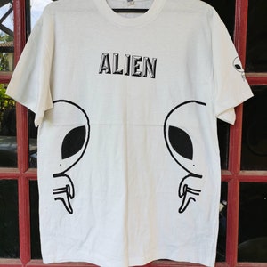 May include: White t-shirt with a black alien graphic and the word "ALIEN" printed on the front.