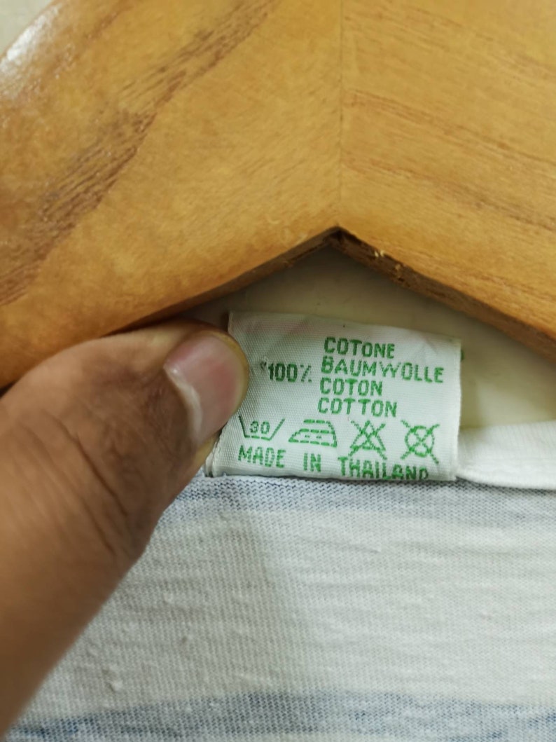 May include: A white and blue striped t-shirt with a green care label that reads "Cotone, Baumwolle, Coton, Cotton, 100%, Made in Thailand".