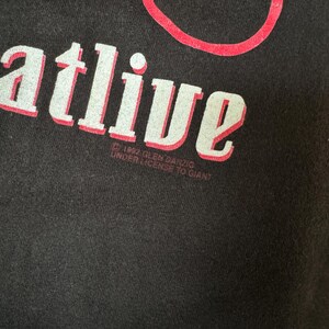 May include: Black t-shirt with white text that reads "You're alive" and red text that reads "&copy; 1994 R.E.M.  SANZIO UNDER LICENSE TO GIANT"