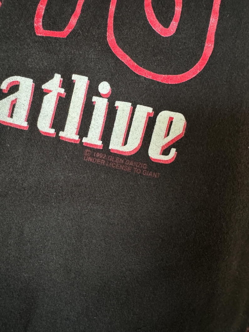 May include: Black t-shirt with white text that reads "You're alive" and red text that reads "&copy; 1994 R.E.M.  SANZIO UNDER LICENSE TO GIANT"