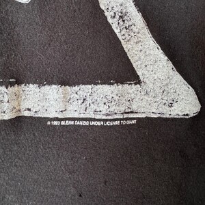 May include: Black t-shirt with a white graphic of a skeleton figure. The text "&copy; 1993 GLENN DANZIG UNDER LICENSE TO GIANT" is printed on the bottom of the shirt.