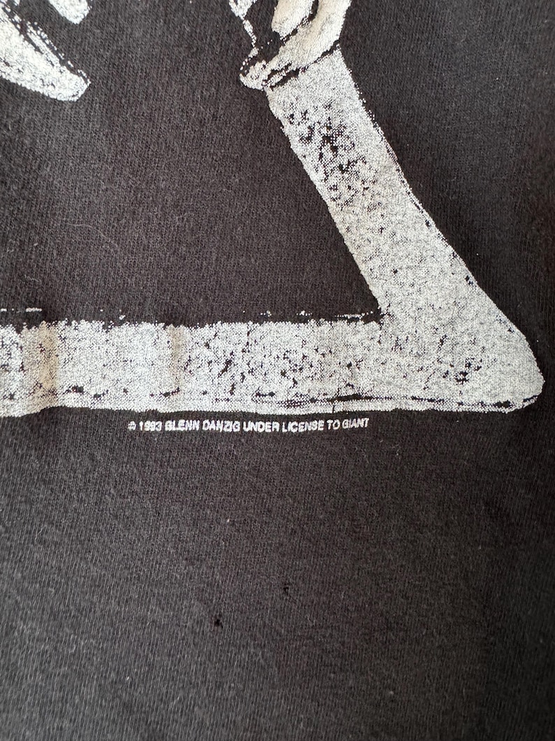 May include: Black t-shirt with a white graphic of a skeleton figure. The text "&copy; 1993 GLENN DANZIG UNDER LICENSE TO GIANT" is printed on the bottom of the shirt.