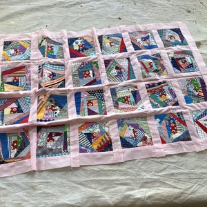 May include: A handmade quilt with a pink border and a patchwork design. The quilt features numerous squares, each showcasing a unique arrangement of colorful fabric scraps in various patterns and hues, creating a vibrant and textured appearance.