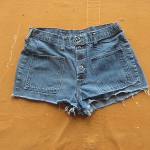 Op de afbeelding: Een blauwe denim short met een knoopsluiting en twee grote zakken aan de voorkant. De short heeft een rafelige zoom.