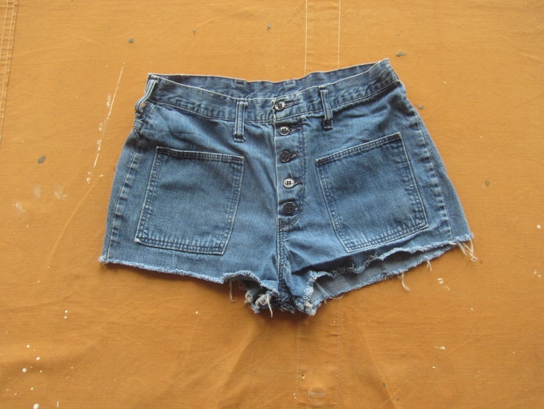 Op de afbeelding: Een blauwe denim short met een knoopsluiting en twee grote zakken aan de voorkant. De short heeft een rafelige zoom.