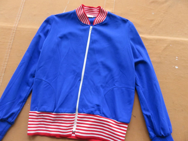 May include: A blue zippered jacket with red and white striped trim around the collar and bottom hem.