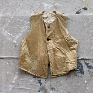 May include: A tan leather vest with a patchwork design. The vest has a button closure and a pointed collar.