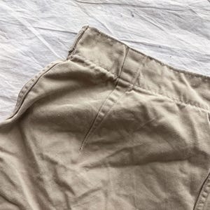 May include: Close-up of tan-colored fabric, possibly part of a garment. The fabric appears to be a sturdy material, with visible stitching along the seams. The image focuses on the waistband and a portion of the garment's side, showcasing the texture and construction.