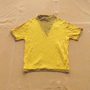 Puede incluir: Una camisa amarilla de manga corta con cuello en V verde.