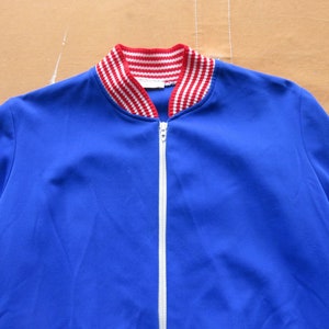 May include: A blue zippered jacket with a red and white striped collar.