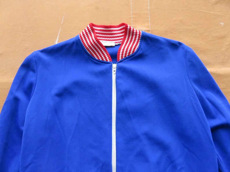 May include: A blue zippered jacket with a red and white striped collar.