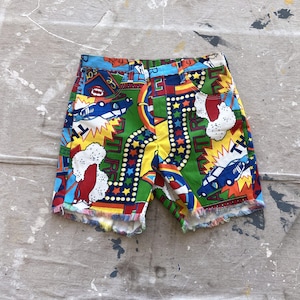 Könnte beinhalten: Eine farbenfrohe Shorts mit einem Retro-Cartoon-Druck mit Autos, Sternen und dem Wort "TIRES". Die Shorts haben einen ausgefransten Saum und sind aus einem leichten Stoff.