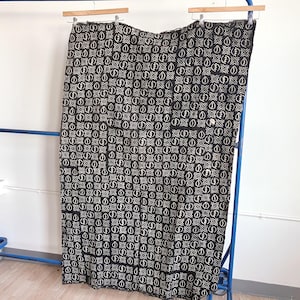 May include: Black and white patterned fabric hanging on a blue clothing rack. The fabric features a repeating geometric design with a central shape surrounded by a square and circular elements. The fabric is draped over a wooden hanger.