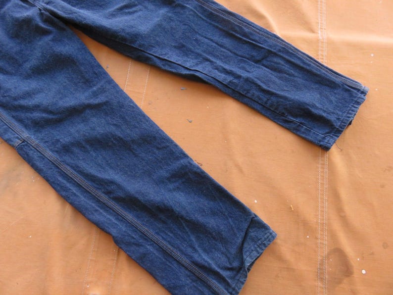 May include: A pair of dark blue denim jeans with a straight leg and a slightly faded appearance. The jeans are laid flat on a brown surface.