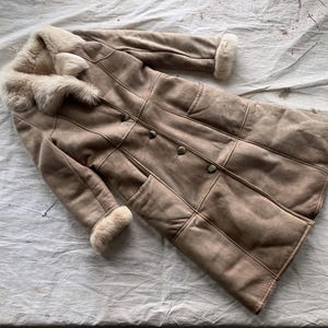 May include: A long, brown suede coat with a white fur collar and cuffs. The coat has a button closure and a few pockets.