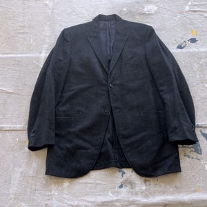 Op de afbeelding: Een donkergrijze blazer met een enkele knoopsluiting en twee zakken. De blazer heeft een subtiel streepjespatroon.