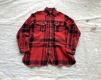 May include: A red and black plaid flannel shirt with two chest pockets and button closures. The shirt has a classic lumberjack style, with a collared neckline and long sleeves. The fabric appears to be a thick, warm material.