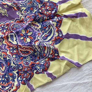 May include: A paisley patterned scarf in shades of purple, red, blue, and yellow. The scarf features a central paisley design with floral accents, surrounded by a yellow border with purple stripes. This accessory is suitable for various occasions.