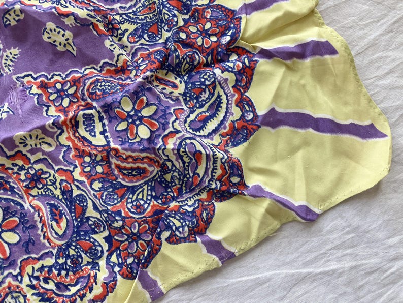 May include: A paisley patterned scarf in shades of purple, red, blue, and yellow. The scarf features a central paisley design with floral accents, surrounded by a yellow border with purple stripes. This accessory is suitable for various occasions.