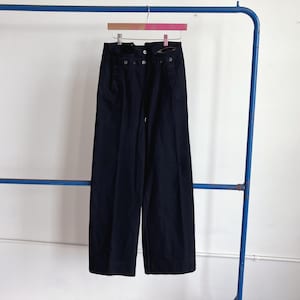 May include: A pair of dark navy blue wide-leg trousers featuring a high-waisted design with a button-front closure. The pants have a structured waistband with visible button details and a clean, straight-leg silhouette that hangs vertically.