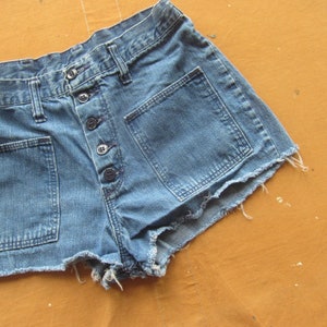 Op de afbeelding: Een lichtblauwe denim short met rafelige randen. De short heeft een knoopsluiting en meerdere zakken.