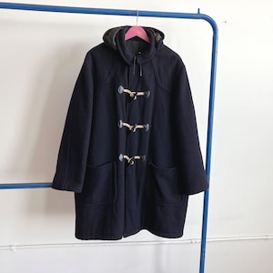 May include: A navy blue duffel coat with a hood, hanging on a pink hanger. The coat features three toggle closures and two front pockets. The coat is made of a thick material, suitable for cold weather.