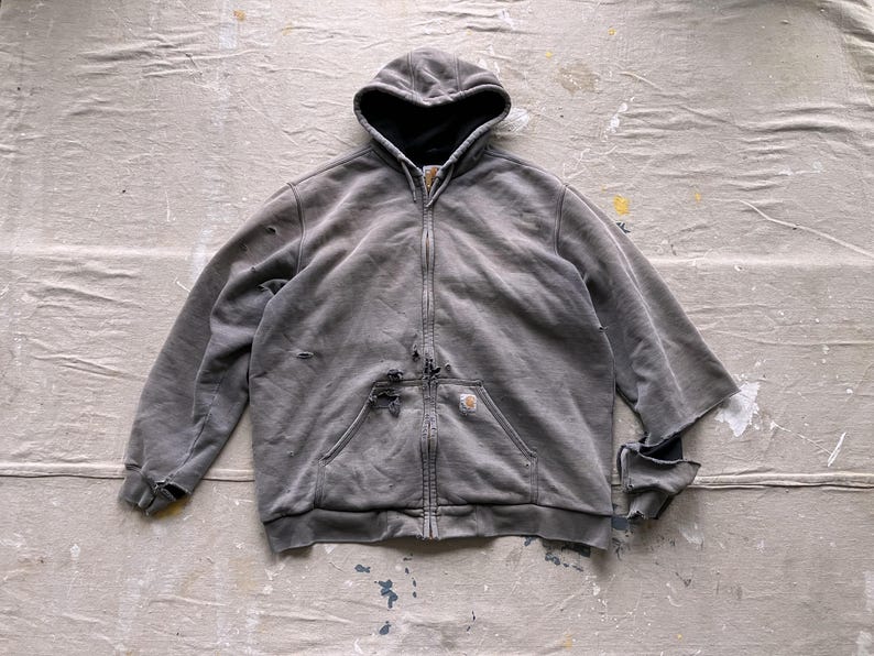 May include: A gray hooded sweatshirt with a zipper closure and a small pocket on the left chest. The sweatshirt has a distressed look with some rips and tears.