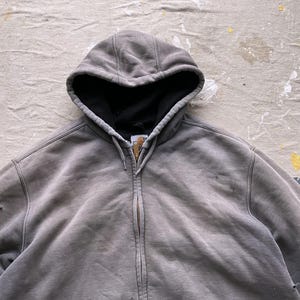 May include: A gray hooded sweatshirt with a zipper closure. The sweatshirt has a faded look and appears to be worn.