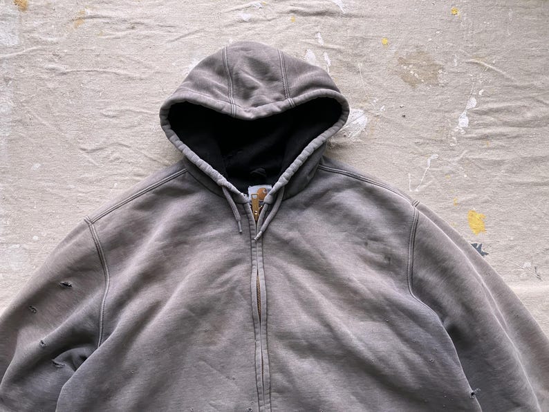 May include: A gray hooded sweatshirt with a zipper closure. The sweatshirt has a faded look and appears to be worn.