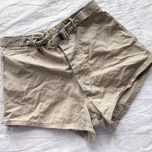 May include: Khaki-colored shorts with a belt and buckle. The shorts have a classic design with a front pocket and a belt loop. The fabric appears to be a durable cotton blend. The shorts are laid flat on a white surface.