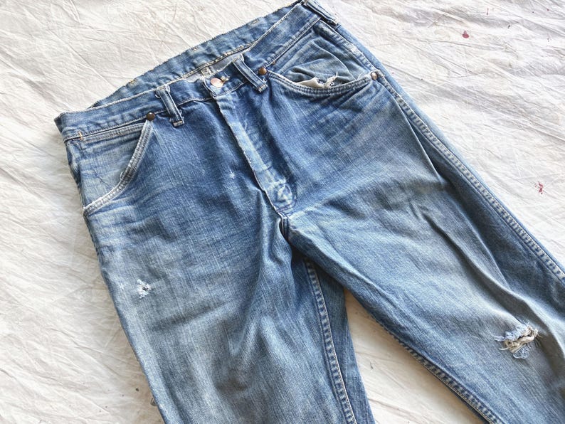 Peut inclure: Jean en denim bleu d&eacute;lav&eacute; avec une conception classique &agrave; cinq poches. Le jean pr&eacute;sente des signes d'usure, notamment des zones ab&icirc;m&eacute;es et un aspect us&eacute;. La couleur bleu clair est uniforme sur tout le v&ecirc;tement.