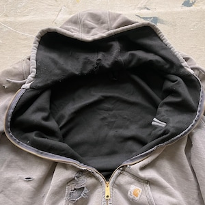 May include: A gray hooded sweatshirt with a black fleece lining. The sweatshirt has a zipper closure and a small logo patch on the front.